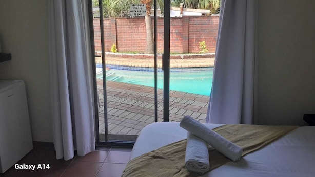 A bedroom with a view of a swimming pool, a Galaxy A14 laptop, and a towel on the bed. - Nqabanqaba B&B  (Richards Bay)