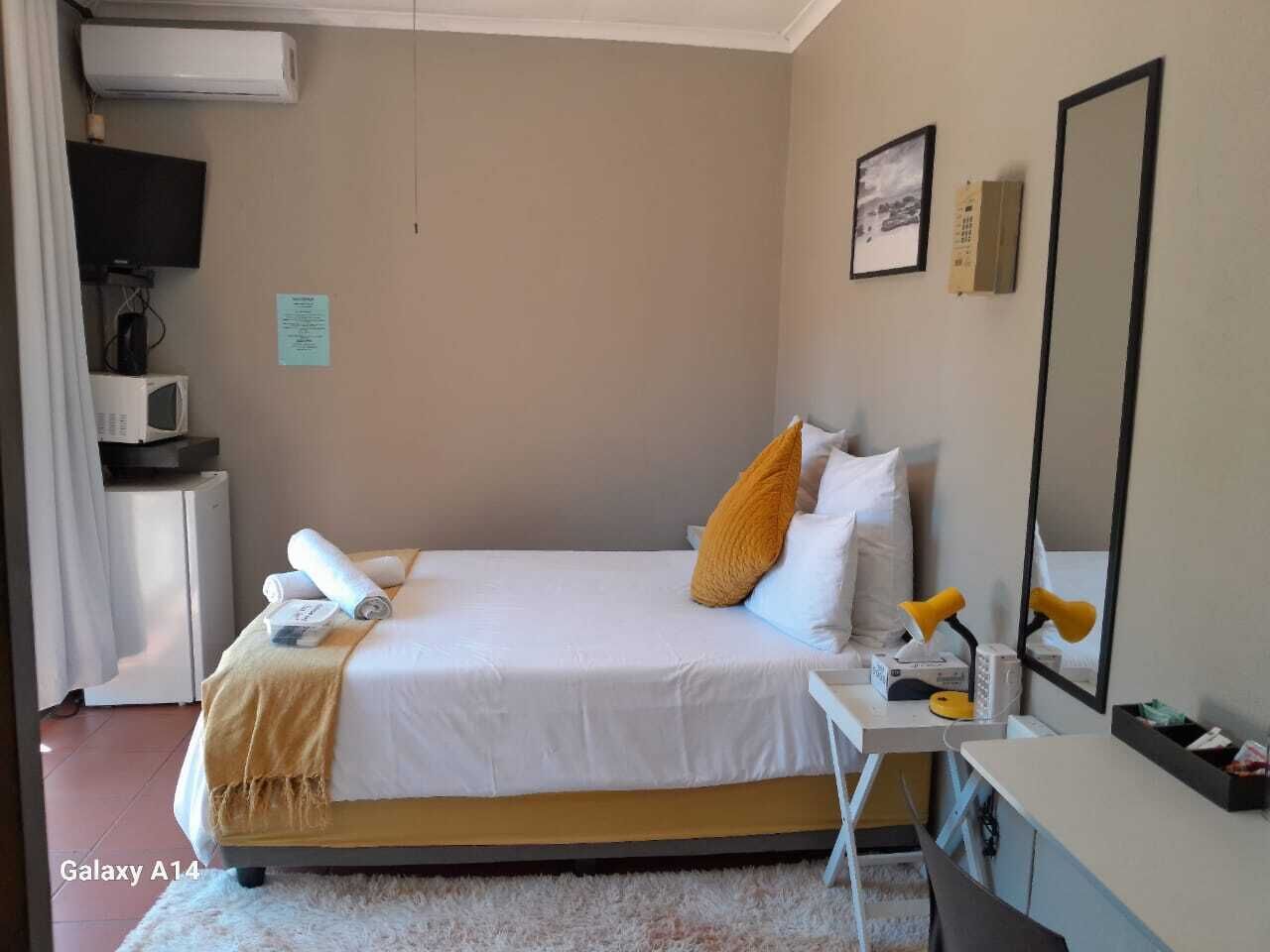 A hotel room with a bed, bedside table, a desk, a chair, a TV, a microwave, and a mirror.