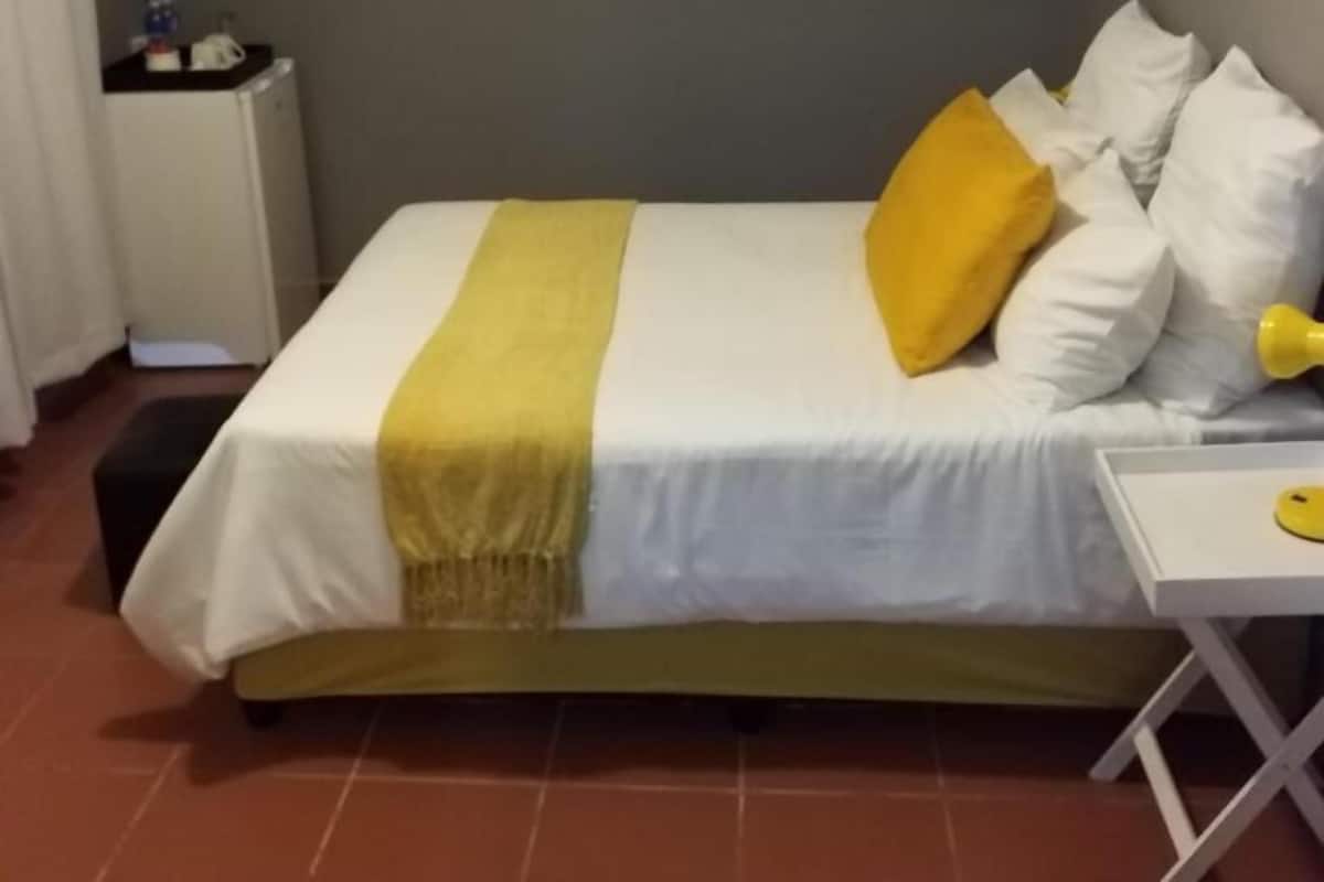 A hotel room with a bed, a bedside table, a TV mounted on the wall, and a radiator.