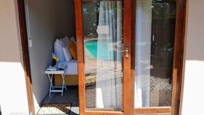 A room with a bed, a small table, and a chair. There is a sliding glass door leading to an outdoor area with a pool. - Nqabanqaba B&B  (Richards Bay)