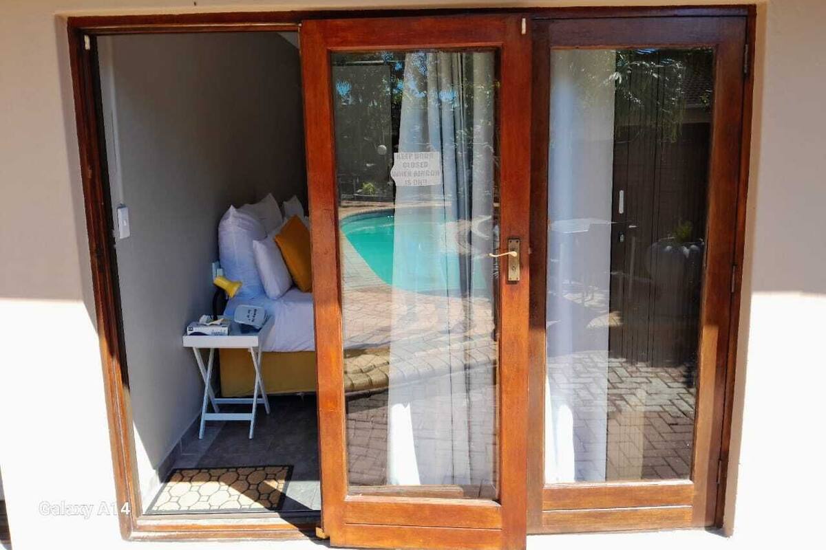 A room with a bed, a small table, and a chair. There is a sliding glass door leading to an outdoor area with a pool.