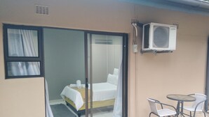 A room with a bed, a small table with chairs, and an air conditioning unit mounted on the wall. - Nqabanqaba B&B  (Richards Bay)