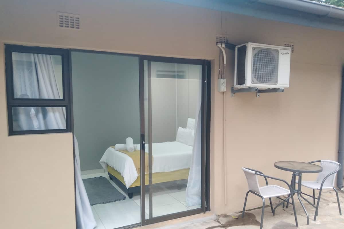 A room with a bed, a small table with chairs, and an air conditioning unit mounted on the wall.