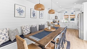 Una cocina moderna con armarios blancos, una mesa de comedor de madera y lámparas colgantes de ratán.
