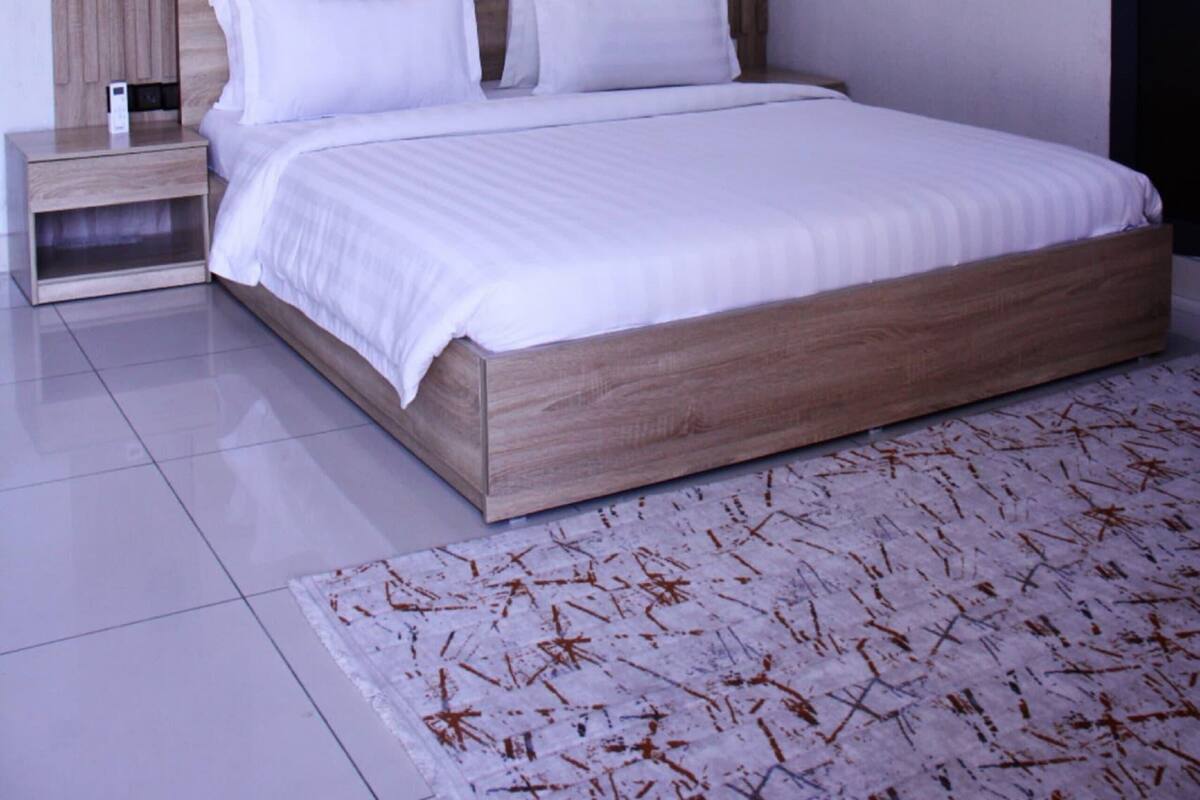 A modern bedroom with a wooden headboard, white bedding, and a framed artwork on the wall.