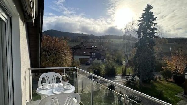 Ein Balkon mit Tisch und Stühlen, der Blick auf eine Wohngegend und Hügel im Hintergrund bietet.