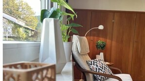 Ein modernes Wohnzimmer mit Holzboden, einem weißen Sofa, einem gemusterten Sessel, einer weißen Lampe und einem Blumentopf.
