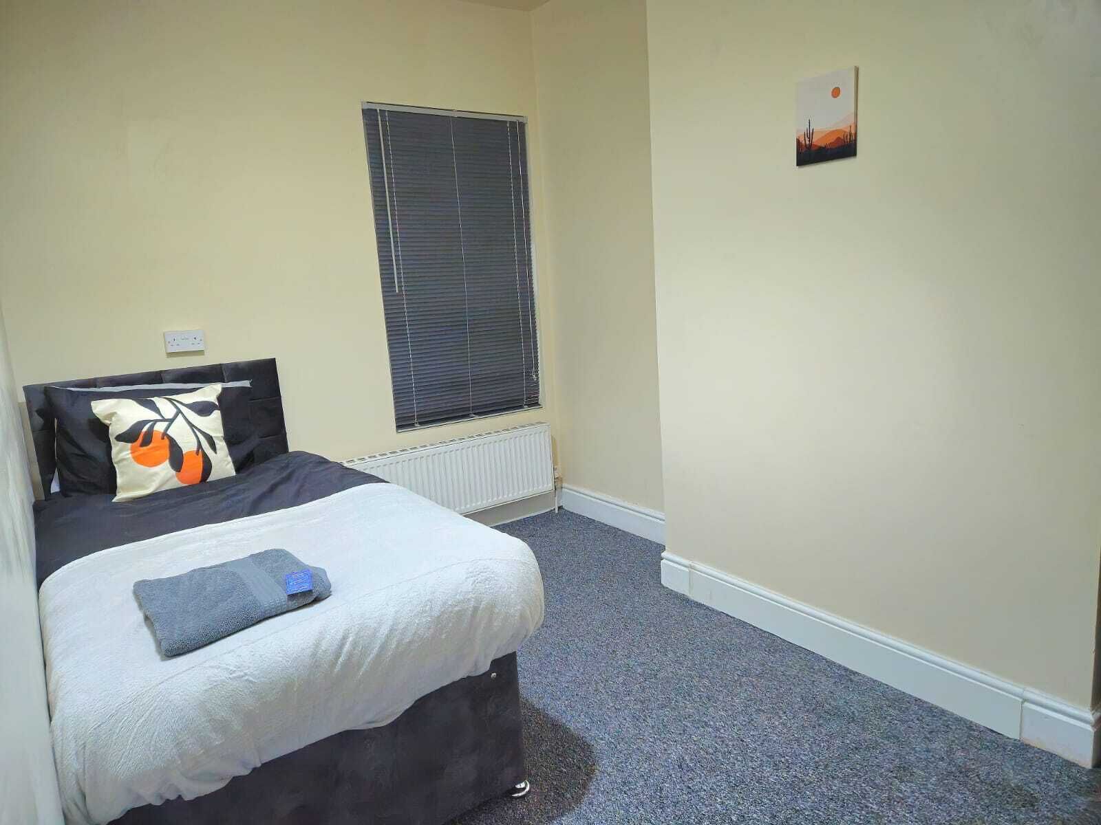 Un dormitorio con cama, una ventana con persianas, un radiador y un cuadro pequeño en la pared.