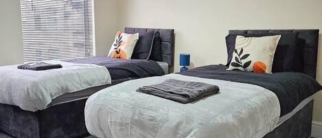 A hotel room with two beds, a large window with blinds, a small wall decoration, and a carpeted floor.