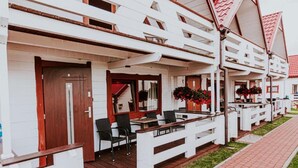 Una hilera de edificios blancos con techos rojos, cada uno con una terraza de madera, mobiliario y macetas.