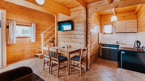 Interior de una cabaña de madera con comedor, cocina y escalera.