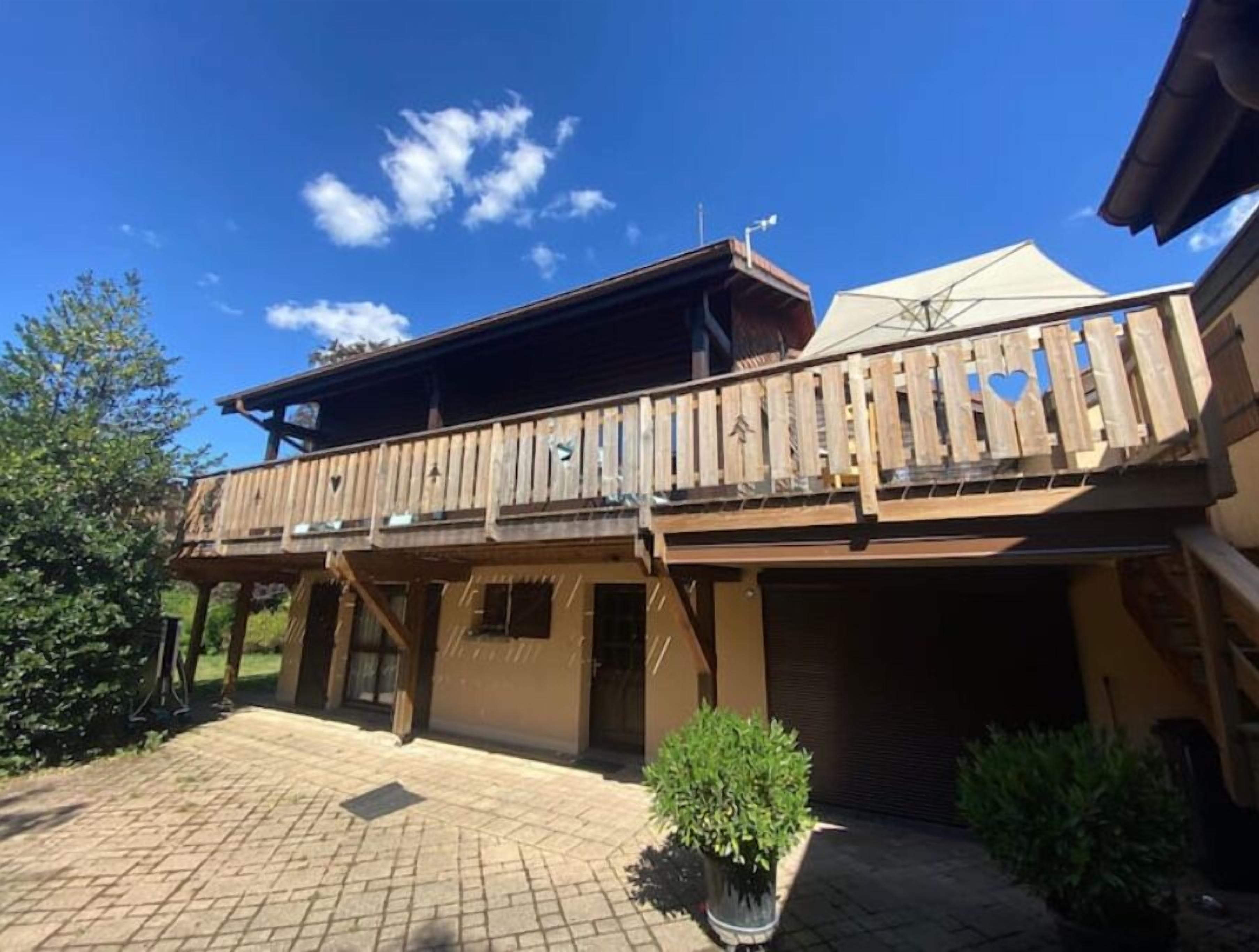 Un bâtiment en bois à deux étages, doté d’un balcon, d’un garage fermé et d’une allée pavée.