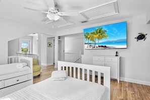 A modern bedroom with a large bed, a ceiling fan, a TV, and a view of a beach. - Anna Maria Island Rental with Saltwater Pool and Elevator - Steps to Beach! (Holmes Beach)