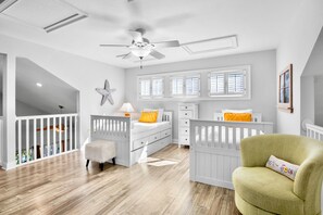 A room with a crib, a chair, a bed, and a window with shutters.