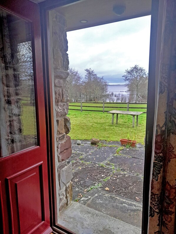 A red door leading to a stone wall and a grassy area with a bench and a small table.