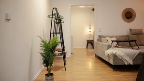 Een woonkamer met een bank, een bijzettafeltje, een vloerlamp en een potplant.