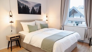 Een slaapkamer met een bed, nachtkastjes, een raam met gordijnen, een radiator en een schilderij aan de muur.