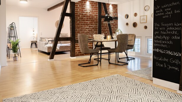 Een moderne woonkamer met een bakstenen muur, houten vloer en een eethoek met tafel en stoelen.