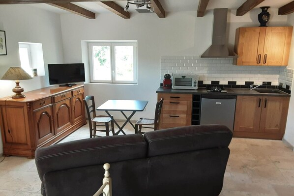 A compact kitchen with wooden cabinets, a dining table, and a sofa. - Stone House in France with Pool & Vineyards (Chambonas)