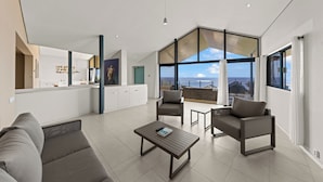 Una sala moderna con un sofá, una mesa de centro y dos sillones. Hay un ventanal que ofrece vistas al mar.