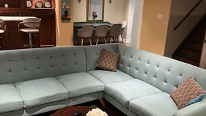 Un salon avec un canapé d’angle bleu clair, une table basse en bois ornée d’un vase de fleurs et un tapis à motifs.