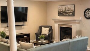 Un salon comprenant un canapé, un fauteuil, un téléviseur, une cheminée et une colonne.