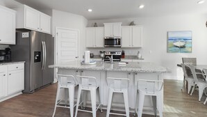 A modern kitchen with white cabinetry, stainless steel appliances, and a central island with bar stools. - Perfect for Groups - Games & Entertainment - Near Beach - Rest Ashored (WindMark Beach)