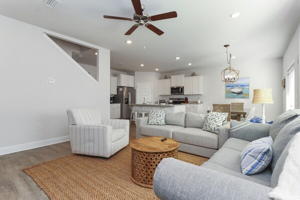 A modern living room with a grey sofa, striped armchair, and a round wooden coffee table. A ceiling fan and recessed lighting are visible. - Perfect for Groups - Games & Entertainment - Near Beach - Rest Ashored (WindMark Beach)