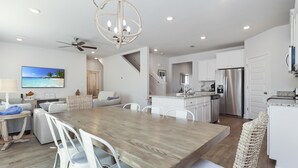A modern kitchen with white cabinets, a stainless steel refrigerator, and a dining area with a wooden table and white chairs. - Perfect for Groups - Games & Entertainment - Near Beach - Rest Ashored (WindMark Beach)