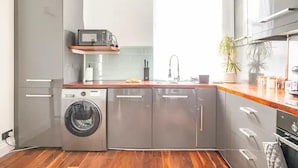 A compact kitchen with a built-in washer, a microwave, and a sink. - Charming 3-bed Apartment in London (London)