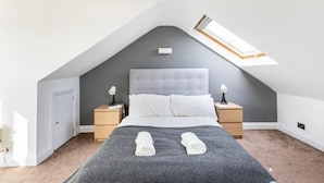 A bedroom with a sloped ceiling, a bed with white linens, two bedside tables with lamps, and a skylight. - Charming 3-bed Apartment in London (London)