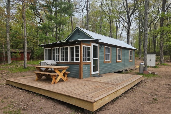 Charming lakeside cabin nestled among towering trees, featuring a spacious deck where you can dine outdoors and soak in nature's tranquility.