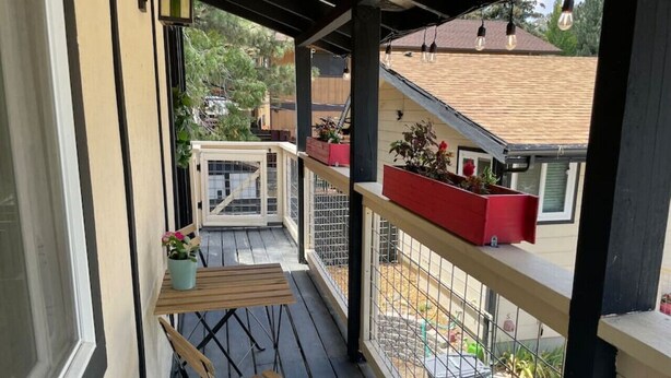 Un balcón cubierto con una mesa y sillas de madera, plantas en macetas y vistas a casas vecinas.