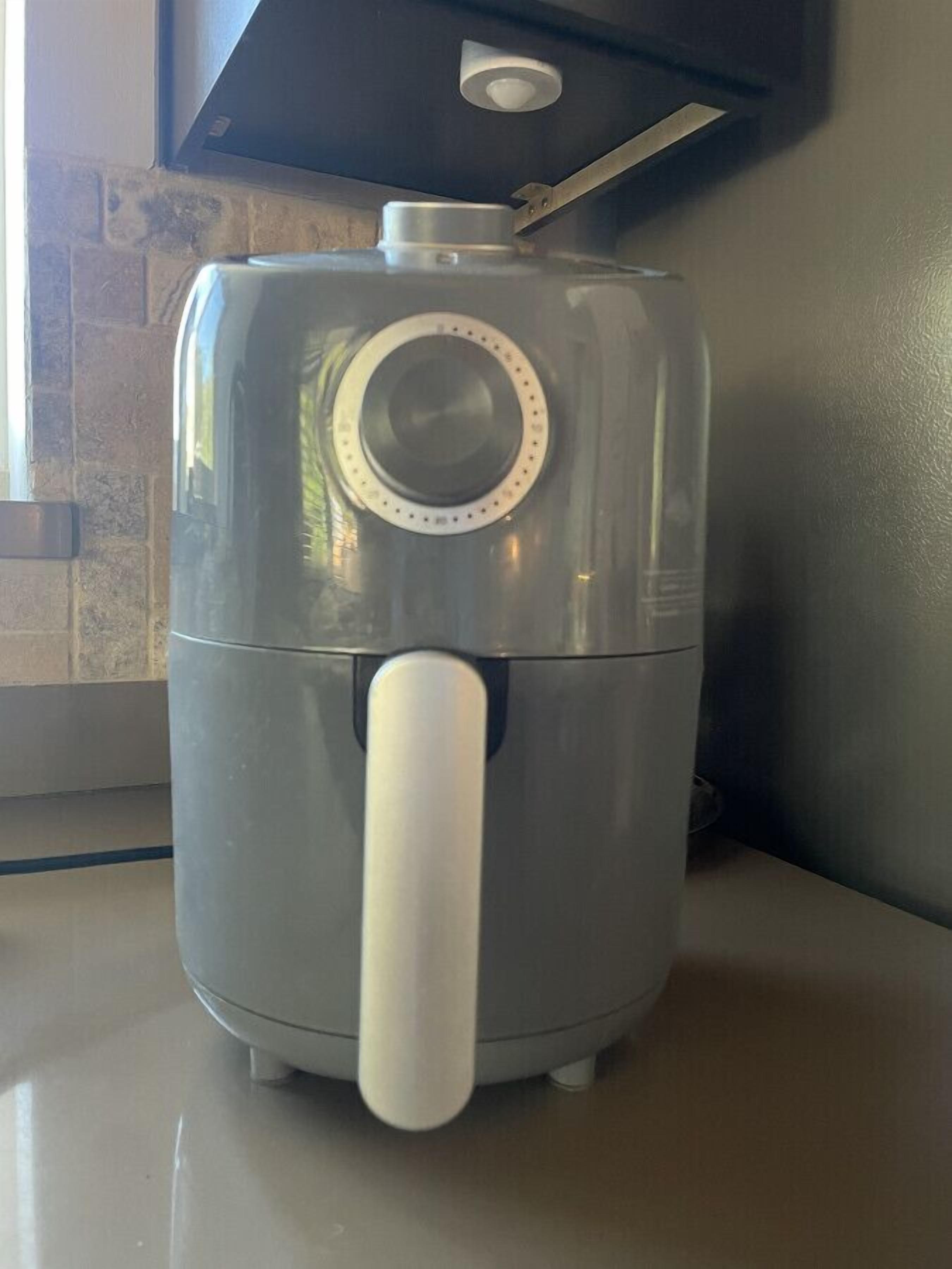 Un appareil de cuisson à air de couleur grise, doté d’un panneau de commande et d’une poignée blanche, posé sur un plan de travail de cuisine.