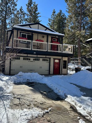 Una casa de dos pisos con garaje, rodeada de nieve y árboles.