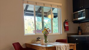 Un comedor con una mesa de madera, dos sillas rojas, un florero con flores y una ventana con persianas.