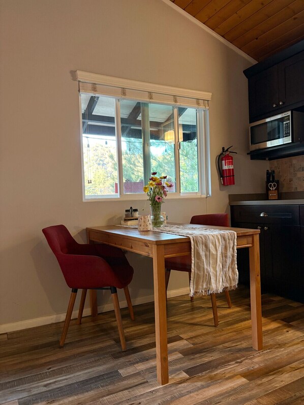 Ein Essbereich mit einem Holztisch, zwei roten Stühlen, einer Blumenvase und einem Fenster mit Jalousien.