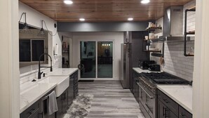 Een moderne keuken met een centraal kookeiland, witte aanrechtbladen en een houten plafond.