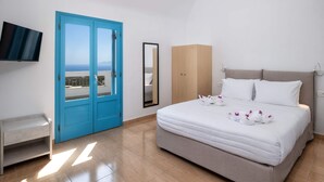 A hotel room with a bed, a blue door, a TV, a mirror, and a wardrobe. - Hillside Elegance  (Santorini)