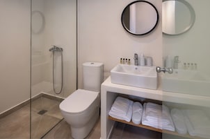 A modern bathroom with a glass-enclosed shower, a toilet, a sink with toiletries, and a shelf with folded towels.
