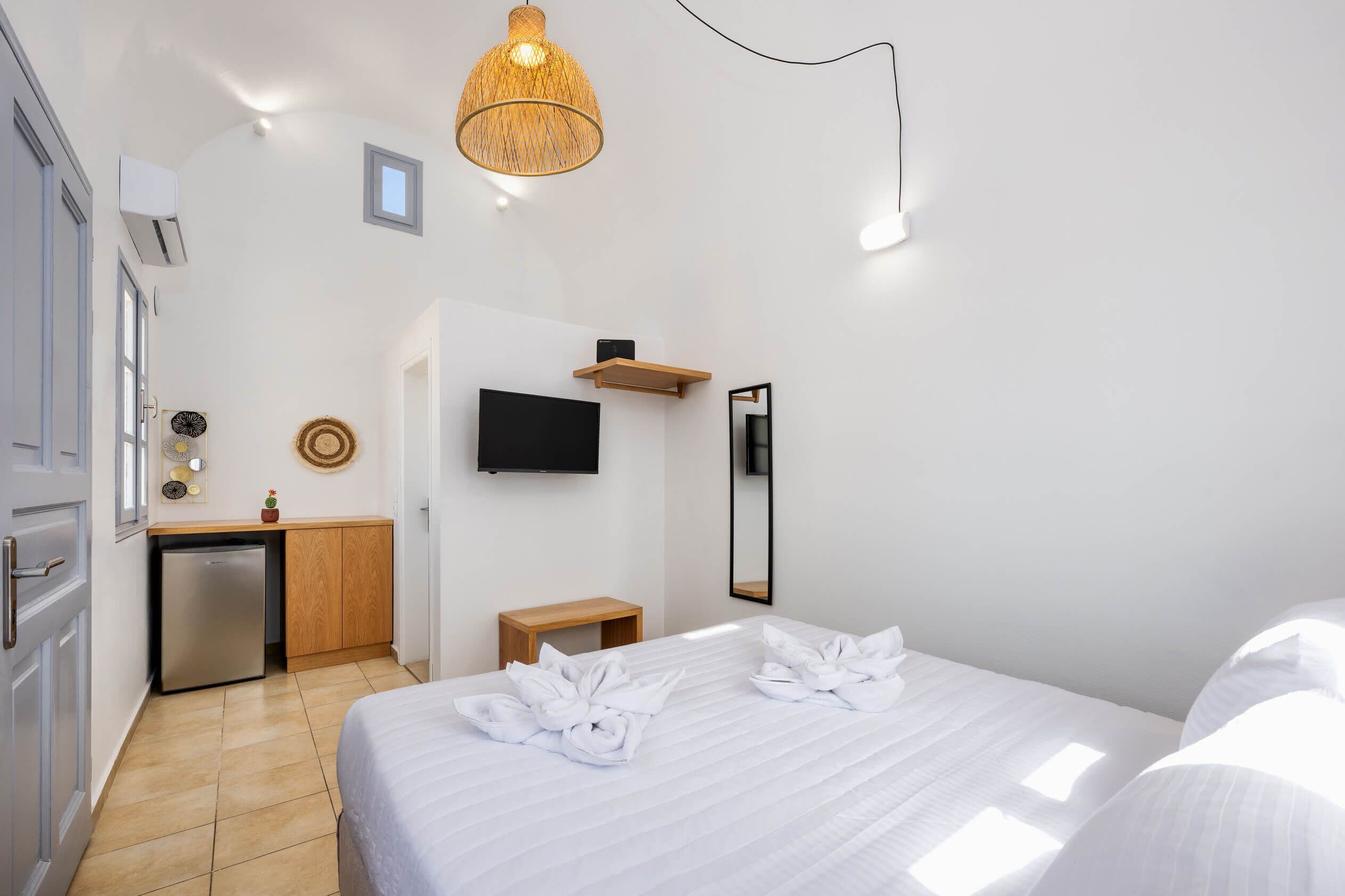 A modern hotel room with a bed, a desk, a television, and a small refrigerator.