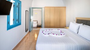 A hotel room with a bed, a wardrobe, a TV mounted on the wall, and a bathroom visible through an open door. - Hillside Elegance  (Santorini)