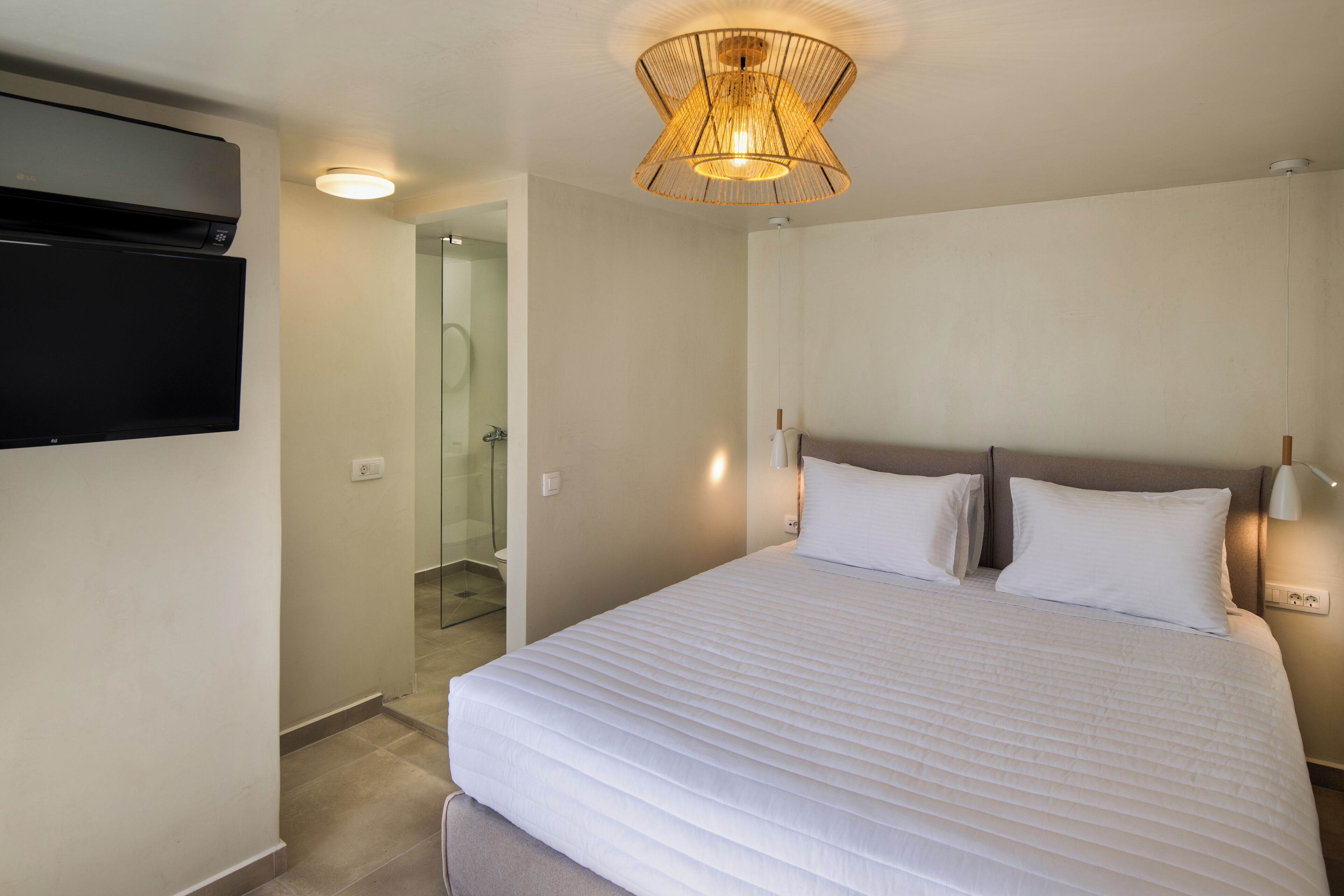 Habitación de hotel con una cama grande, un televisor de pantalla plana montado en la pared y una lámpara colgante moderna.