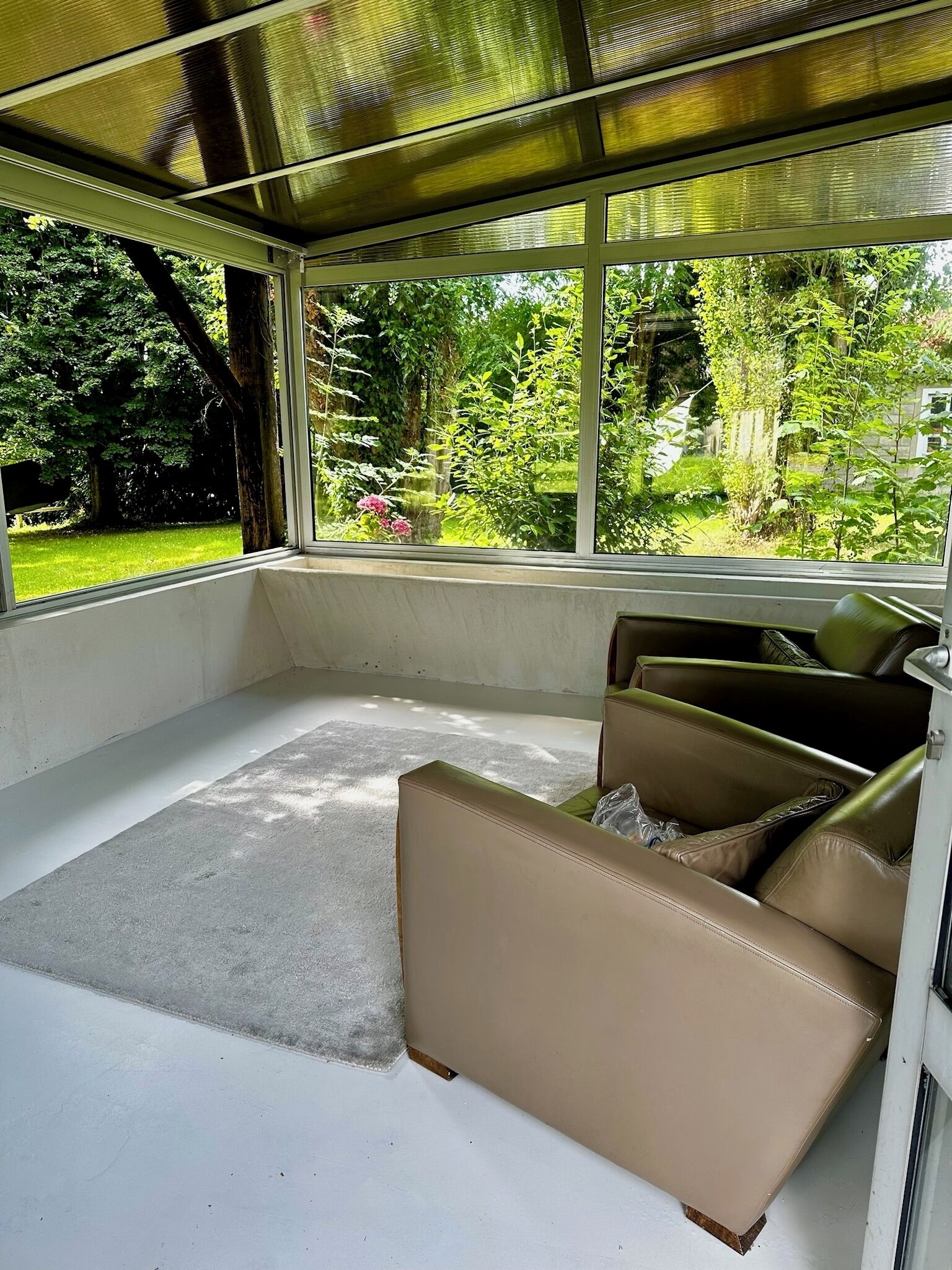 A sunroom with a large window, a beige sofa, and a white carpet.