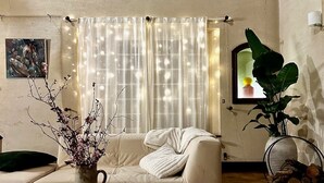A living room with a sofa, a coffee table, a colorful rug, a potted plant, and a window with curtains. - Domaine Verneuil, un Havre de Paix Dans Le Perche (La Chapelle-Souëf)