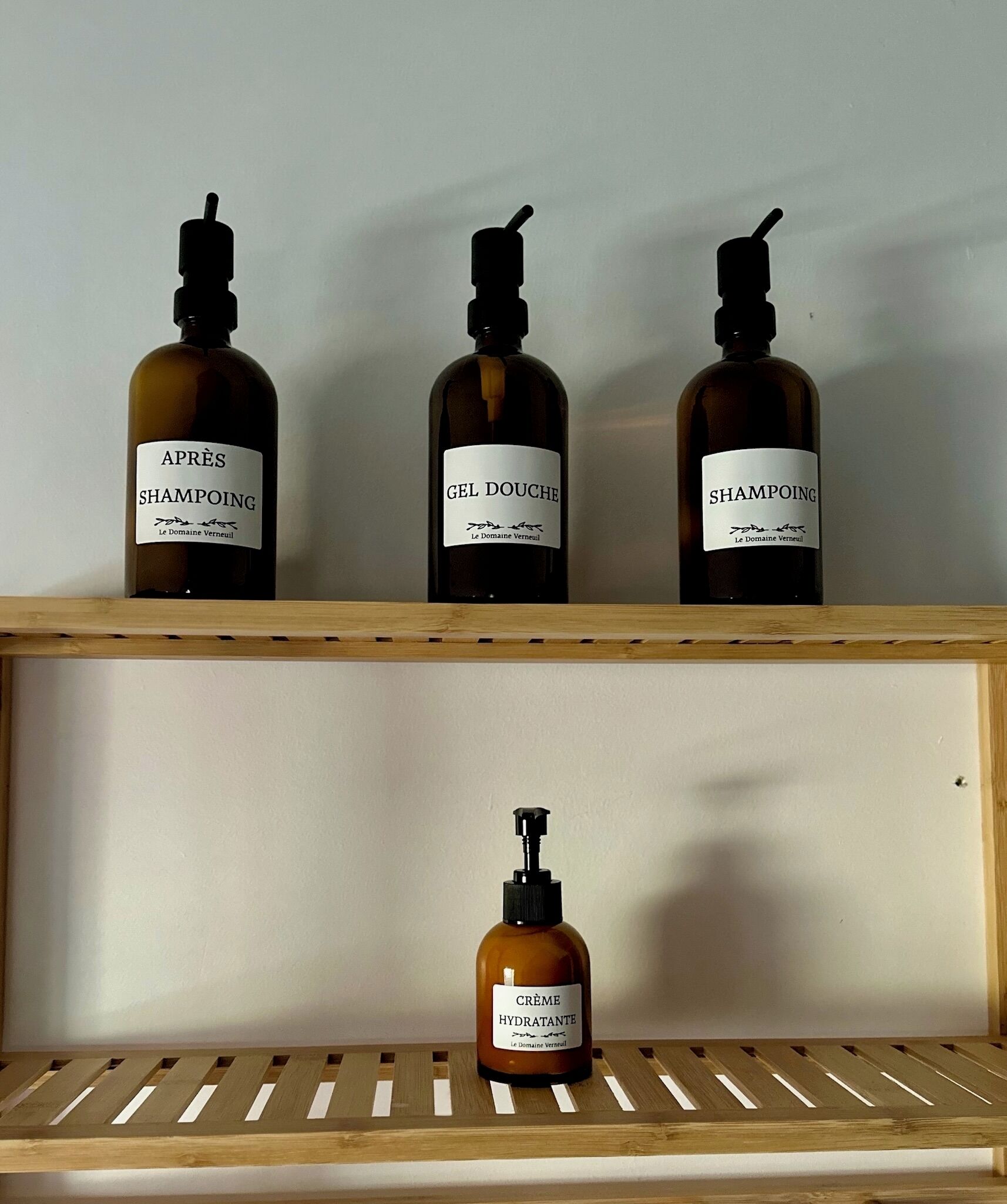Tres botellas de productos para el cabello sobre un estante de madera frente a una pared lisa.