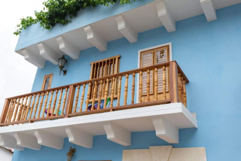 A blue building with a wooden balcony, white railings, and a small window.