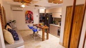 A compact living space with a kitchenette, a dining area with a blue chair, and a sofa with cushions. - Casa Azul 1 💙 El Espinal (Cartagena de Indias)