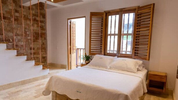 A bedroom with a bed, wooden shutters, a nightstand, and a staircase. - Casa Azul 1 💙 El Espinal (Cartagena de Indias)