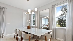 A dining area with a large white table, six chairs, a chandelier, and a large mirror. - 5BR townhouse with pool near Disney area (Kissimmee)